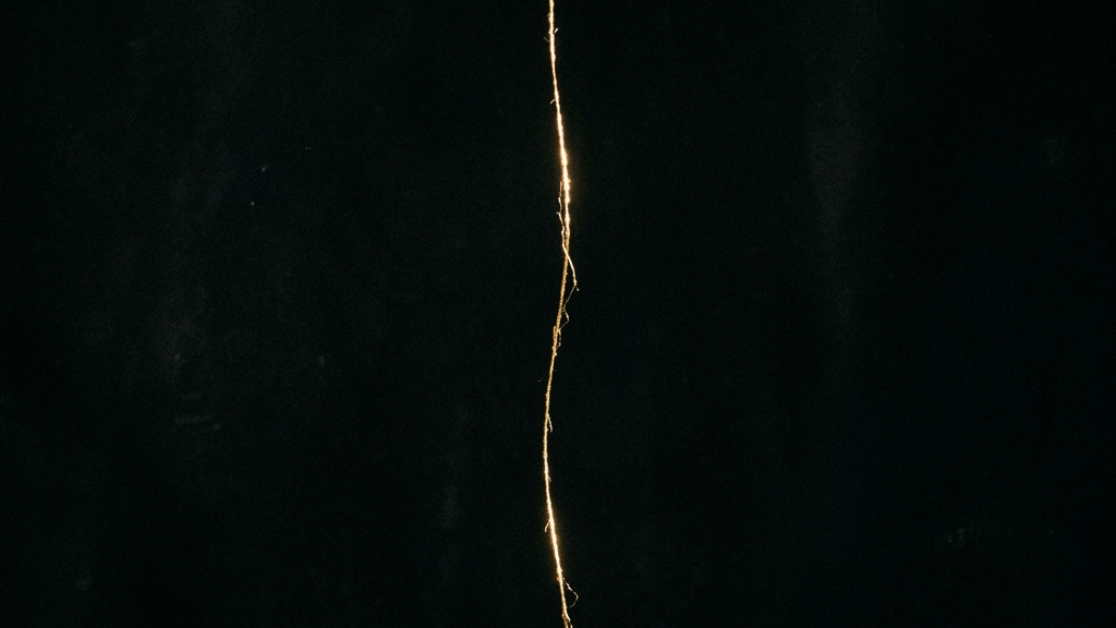 静寂の闇の中、柔らかな光を反射する一本の繊細な金糸が描く価値のパラドックス