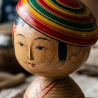 鮮烈な染料によって彩られる弥治郎こけしの頭部と白木の質感